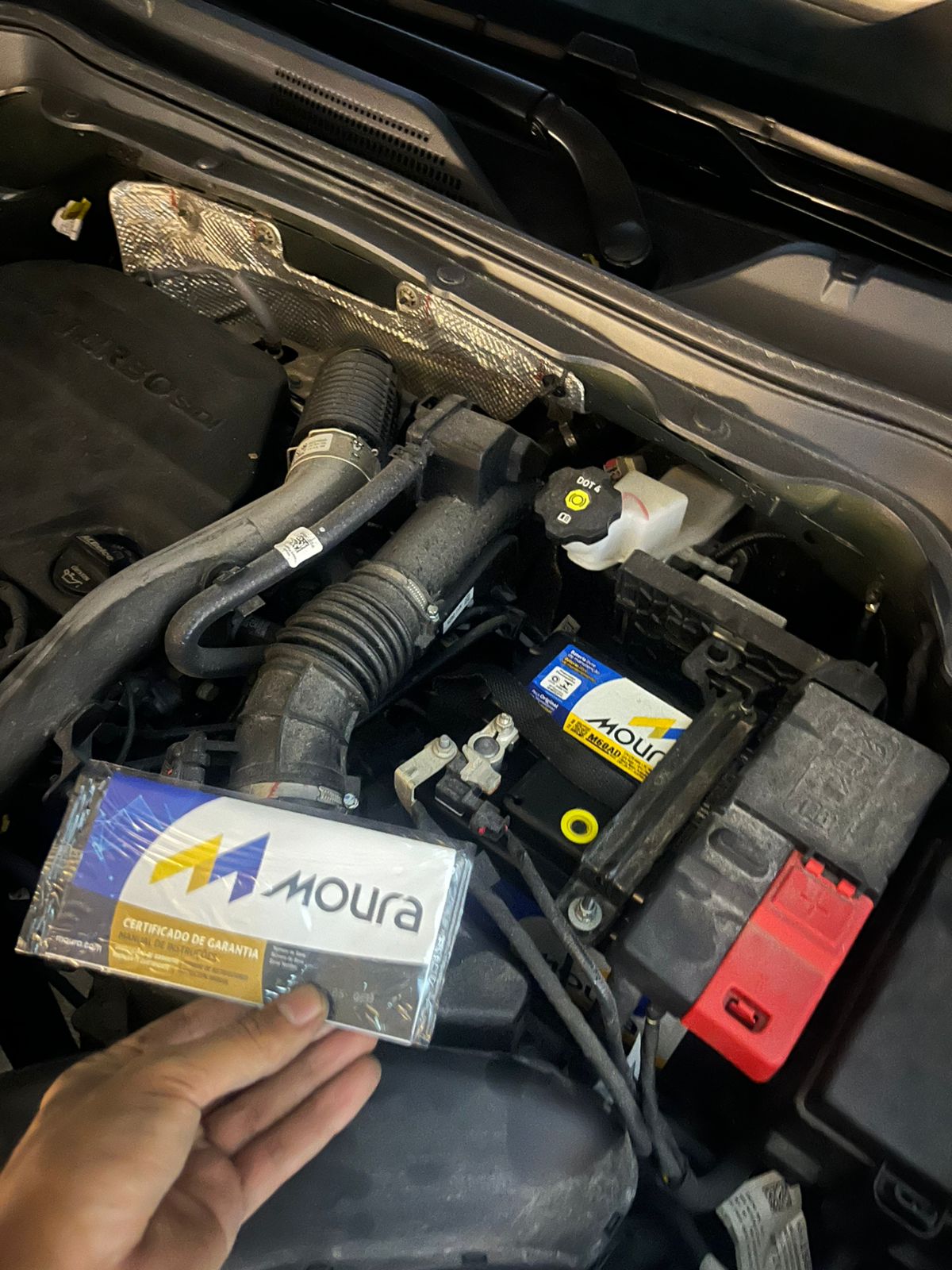 Bateria automotiva instalada em veículo com manual de garantia em mãos